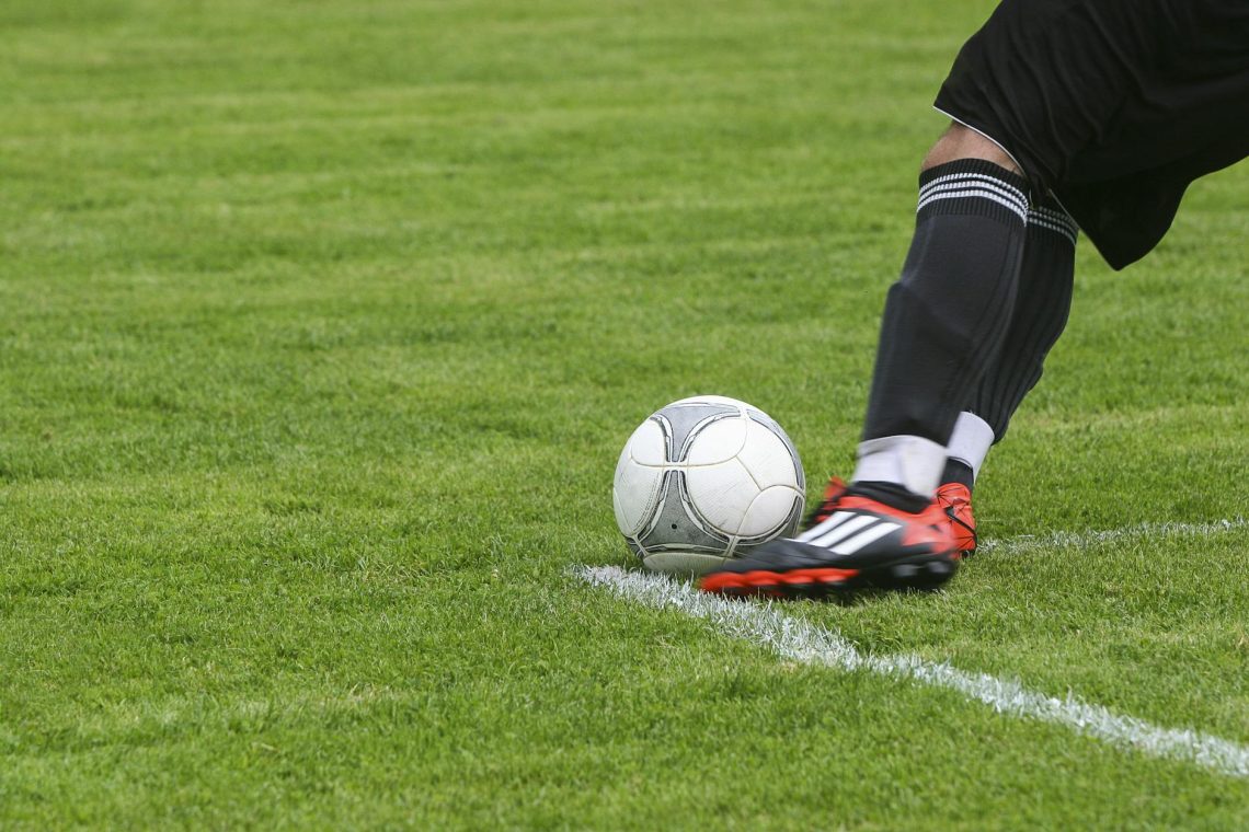 soccer player kicking white gray soccer ball on green grass field